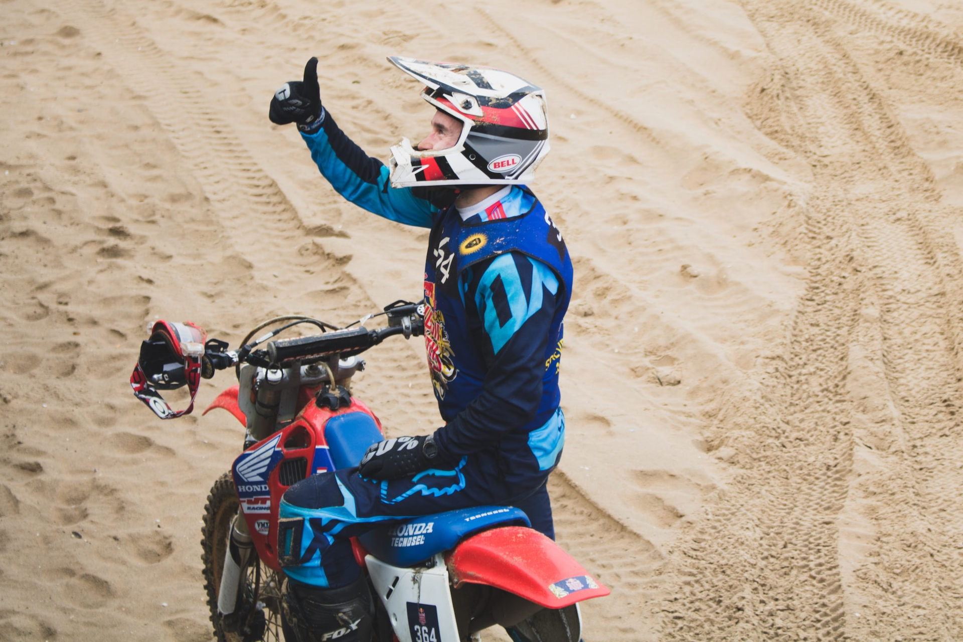 Motard avec un casque cross posant sur sa moto pouce en l'air